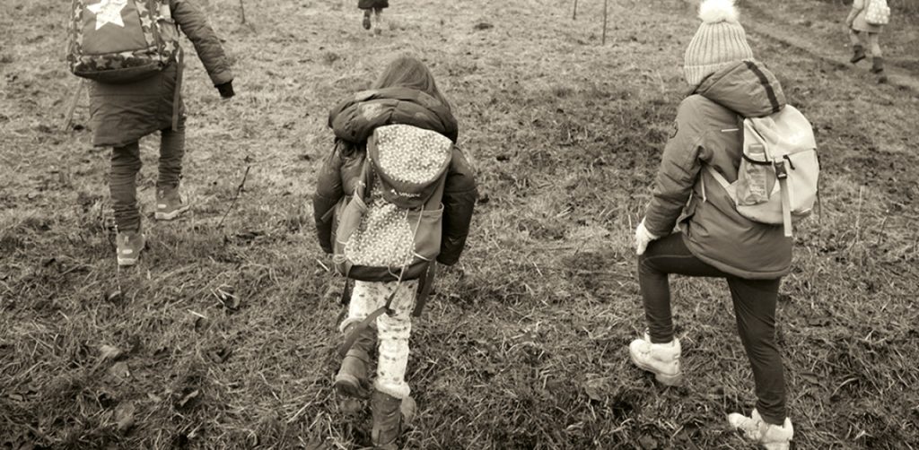 Drei Kinder mit Rucksäcken laufen gemeinsam über eine Wiese